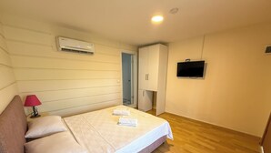 A bedroom with a bed, pillows, a bedside lamp, an air conditioning unit, a wardrobe, and a television. - Address Küçükkuyu (Ayvacik)