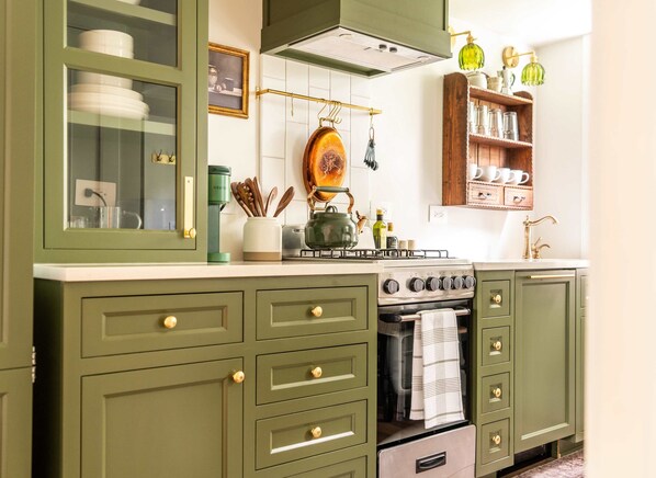 Una cocina con gabinetes verdes, estufa, horno y un colgador para ollas.