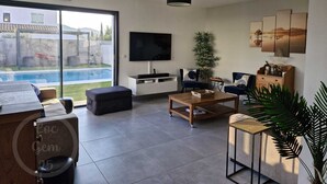 Een moderne woonkamer met een televisie, zitplaatsen, een salontafel en uitzicht op een zwembad.