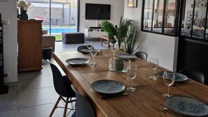 Een moderne eethoek met een houten tafel voor zes personen, een televisie en een groot raam met uitzicht op een zwembad.