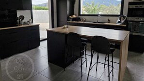 Een moderne keuken met een centraal eiland, zwarte keukenkastjes en een groot raam met uitzicht op groen en heuvels.