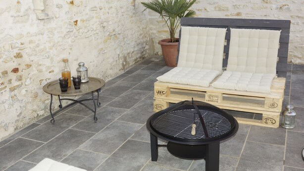 A rustic outdoor seating area with a wooden bench, a small round table with drinks, and a potted plant.