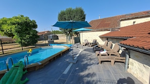 Una piscina con uno scivolo, lettini e una zona coperta con un ombrellone.