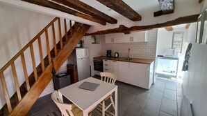 Cuina amb armaris blancs, una escala de fusta i zona de menjador amb taula i cadires.