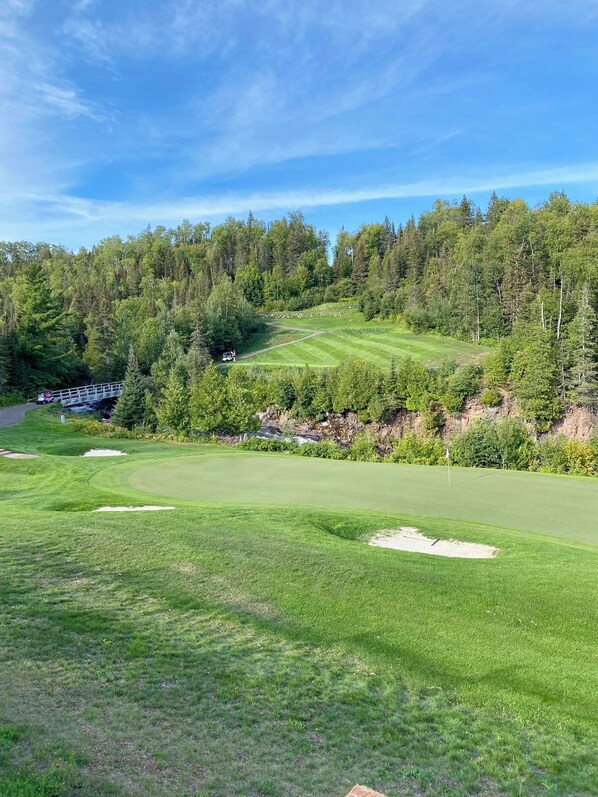 A golf course with a bridge, trees, and a clear sky.