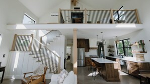 Un loft spacieux avec une mezzanine, une cuisine équipée d’appareils électroménagers modernes et un coin repas agrémenté de tabourets de bar.