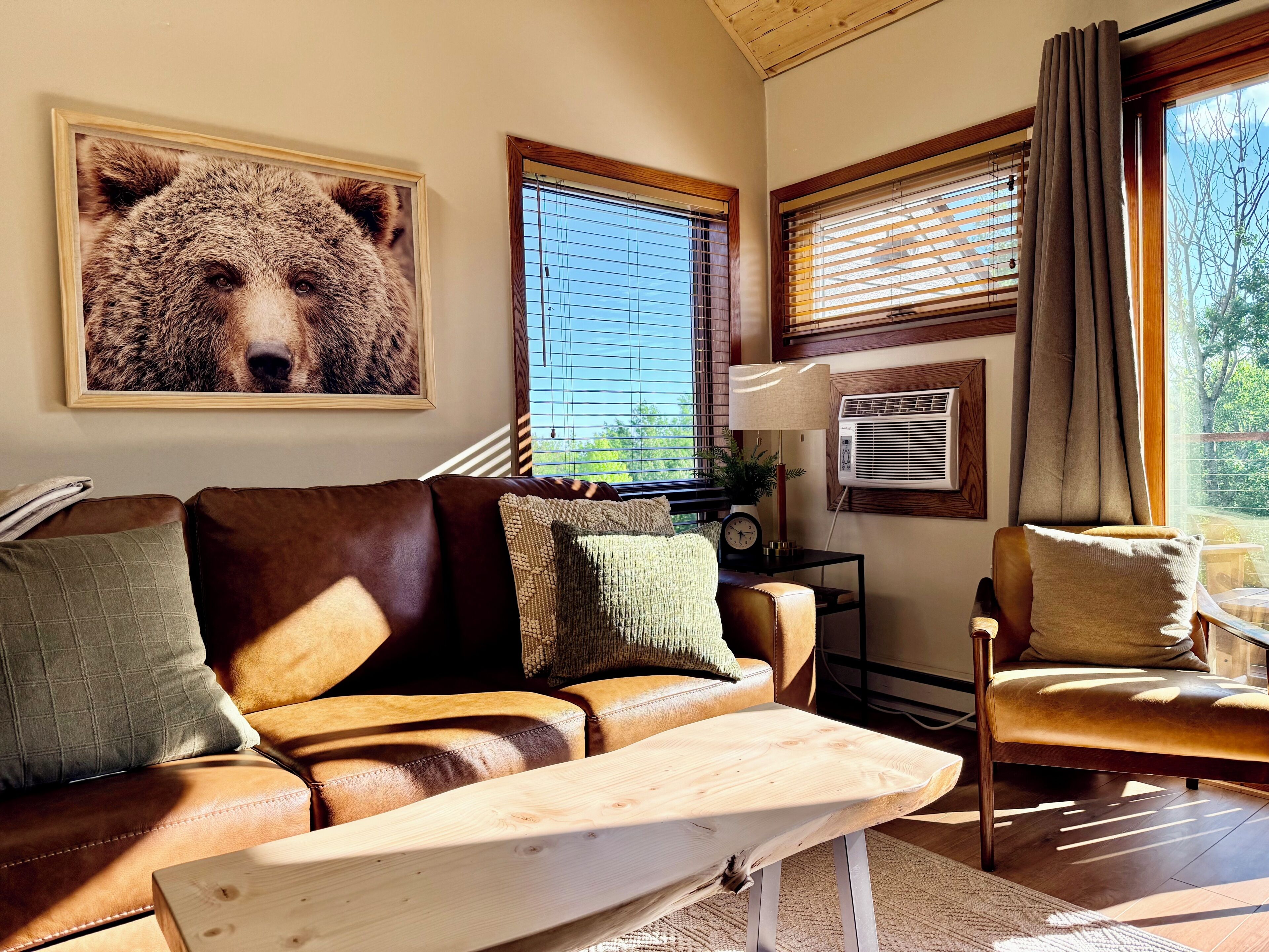 A cozy living room with a brown leather sofa, a wooden coffee table, and a large bear painting on the wall.