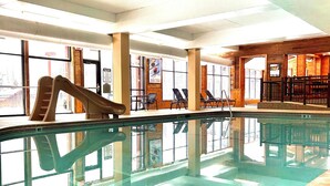 An indoor swimming pool with a slide, seating areas, and large windows.