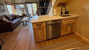 A modern kitchen with wooden cabinets, a stainless steel dishwasher, and a large window.