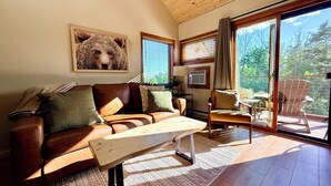 A cozy living room with a leather sofa, a wooden coffee table, and a large window with a view of trees.