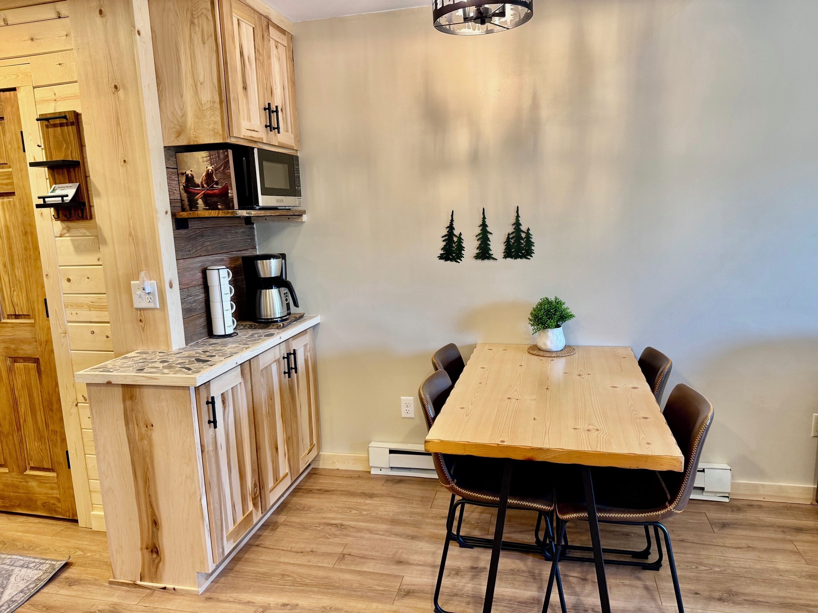 A kitchen with wooden cabinets, a microwave, a coffee maker, and a dining table with chairs.