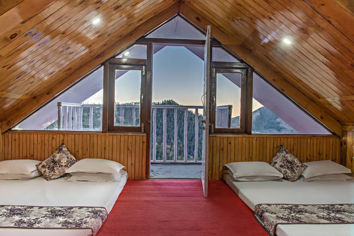 A cozy attic bedroom with two beds, a red carpet, and large windows offering a view of the forest.