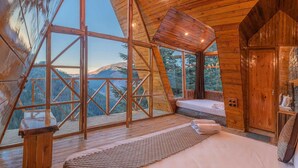 Eine Holzhütte mit einem großen Bett, einem kleinen Badezimmer und einem Balkon mit Blick auf die Berge.