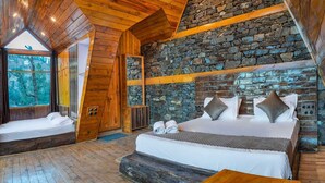 Ein rustikales Holzhäuschen mit einer Steinwand, einem großen Bett mit Kissen und Blick auf den Wald durch ein Fenster.