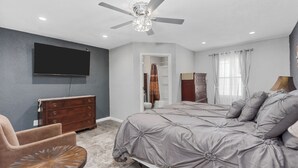 A bedroom with a bed, a dresser, a TV, a ceiling fan, and a chair.