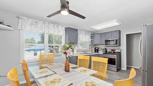 A modern kitchen with grey cabinets, a stainless steel refrigerator, and a dining area with yellow chairs and a glass table.
