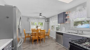 A modern kitchen with a dining area, grey cabinets, a stainless steel refrigerator, and a black stove.