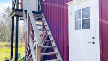Una escalera de madera que lleva a una puerta blanca con un ventanal, junto a un edificio rojo.