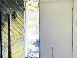 Een houten deur met een verweerde afwerking, een veranda met een leuning en een zichtbaar buitengebied.