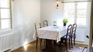 Un comedor con una mesa lista para cuatro, sillas de madera, un radiador y una ventana con cortinas.
