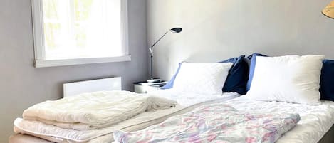 A bedroom with two beds, a bedside table with a lamp, and a window with curtains.