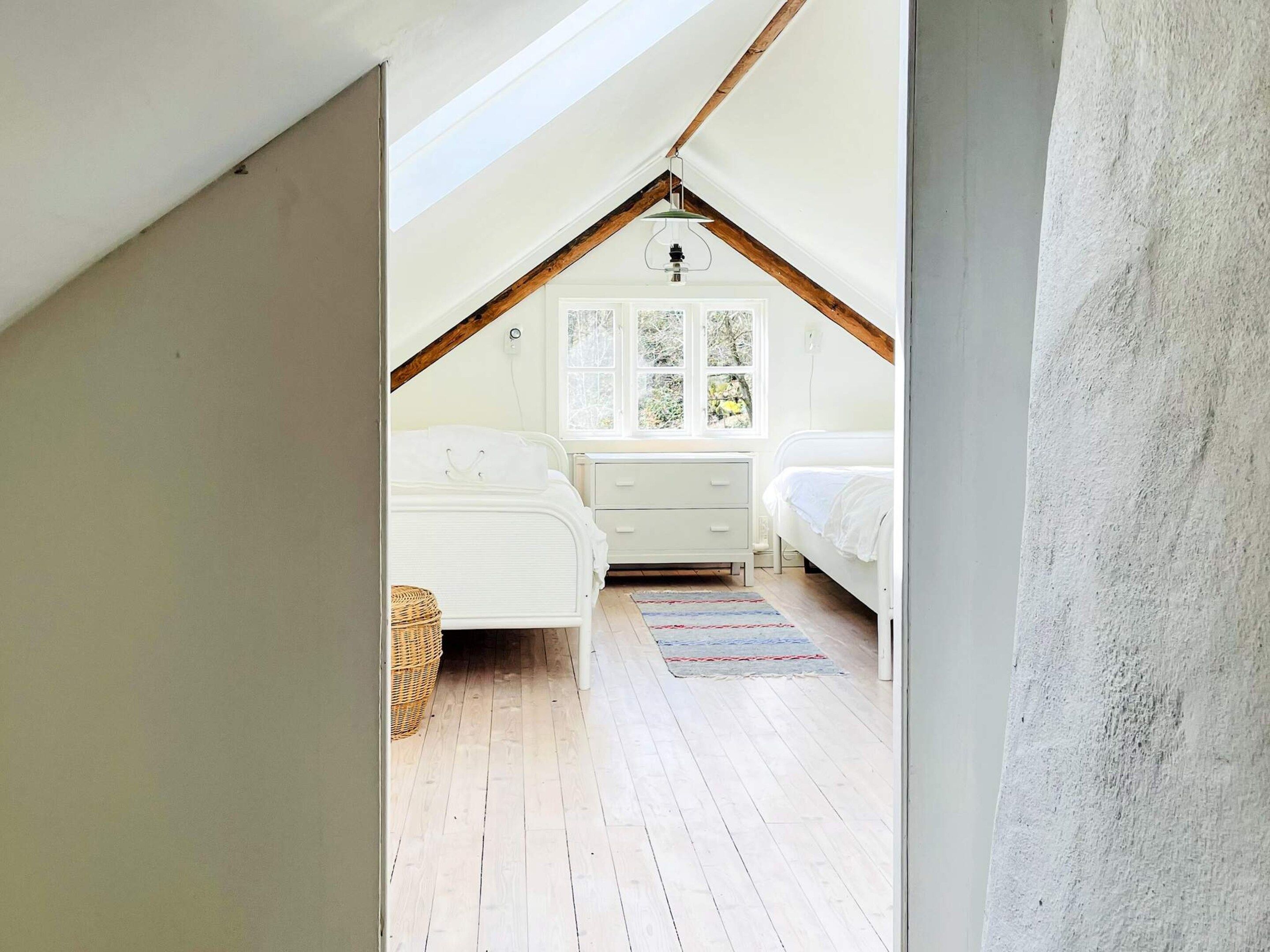 Un dormitorio con techo inclinado, ventana con vistas, cama, mesita de noche y cómoda.