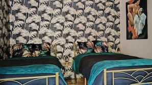 Une chambre avec deux lits, un rideau à motifs et un tableau au mur.