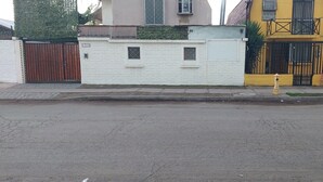 Une vue de rue avec une entrée fermée par un portail, un bâtiment blanc doté de petites fenêtres et un bâtiment jaune avec un portail noir.