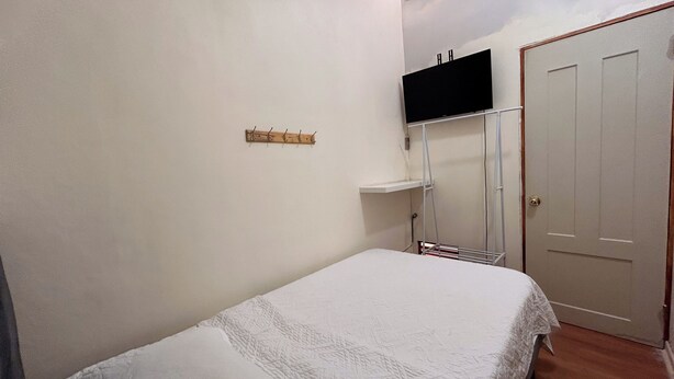 Une chambre à coucher avec un lit, un porte-manteau, un téléviseur fixé au mur et une porte.