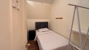 Une petite chambre à coucher, bien rangée, avec un lit simple, une table de chevet et une armoire.