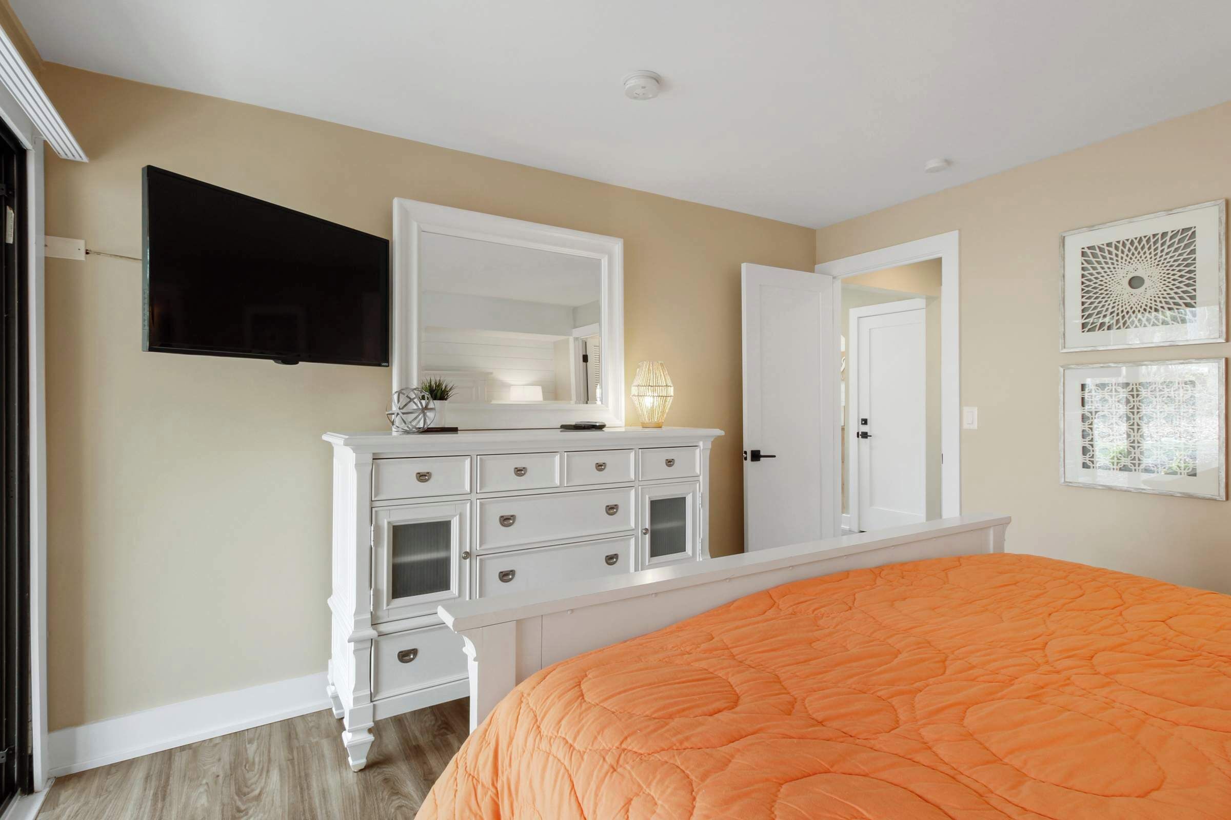 A bedroom with a large bed, a dresser, a television mounted on the wall, and two doors.