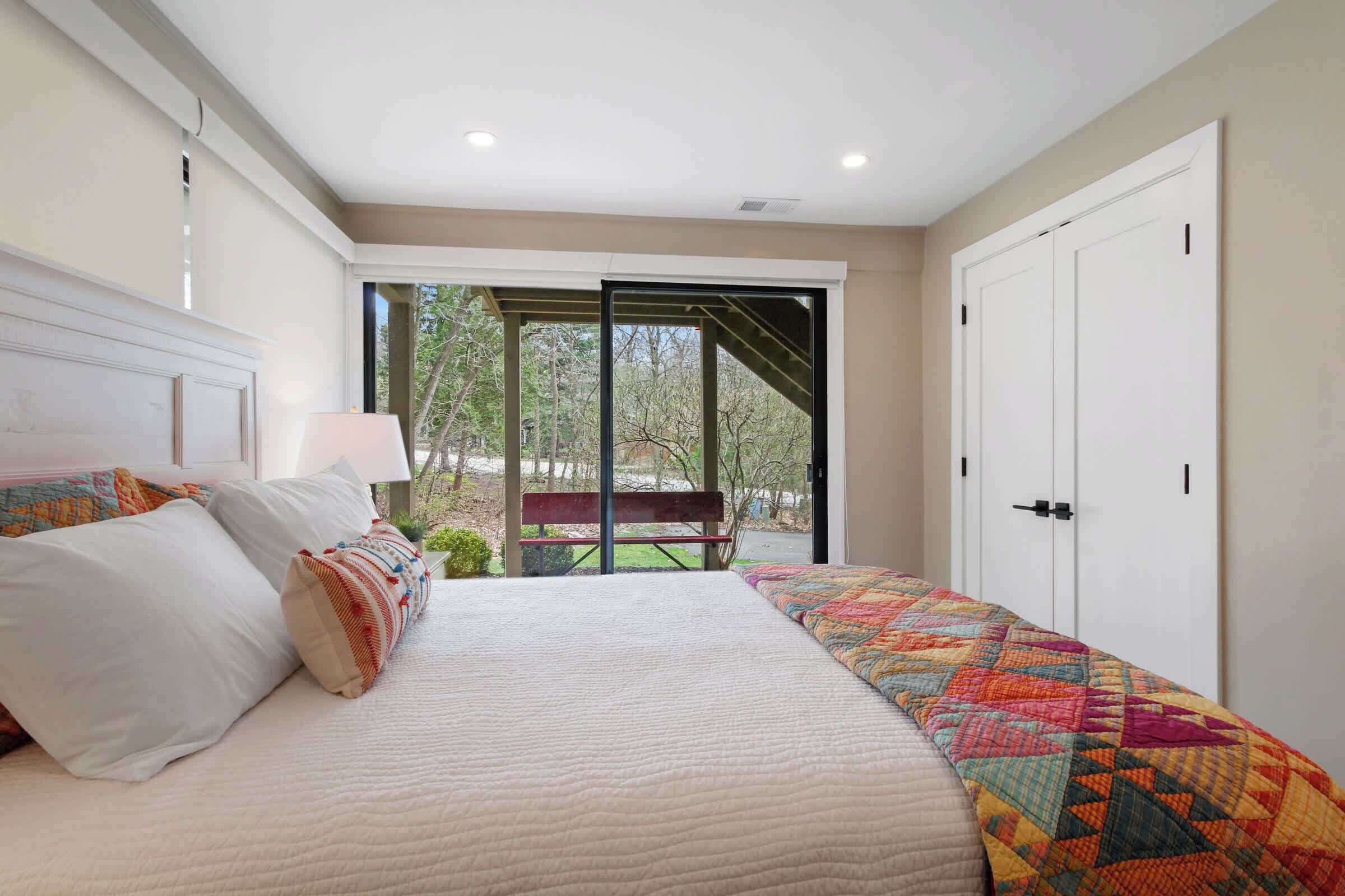 A bedroom with a large bed, a bench outside the door, and a view of the outdoors.