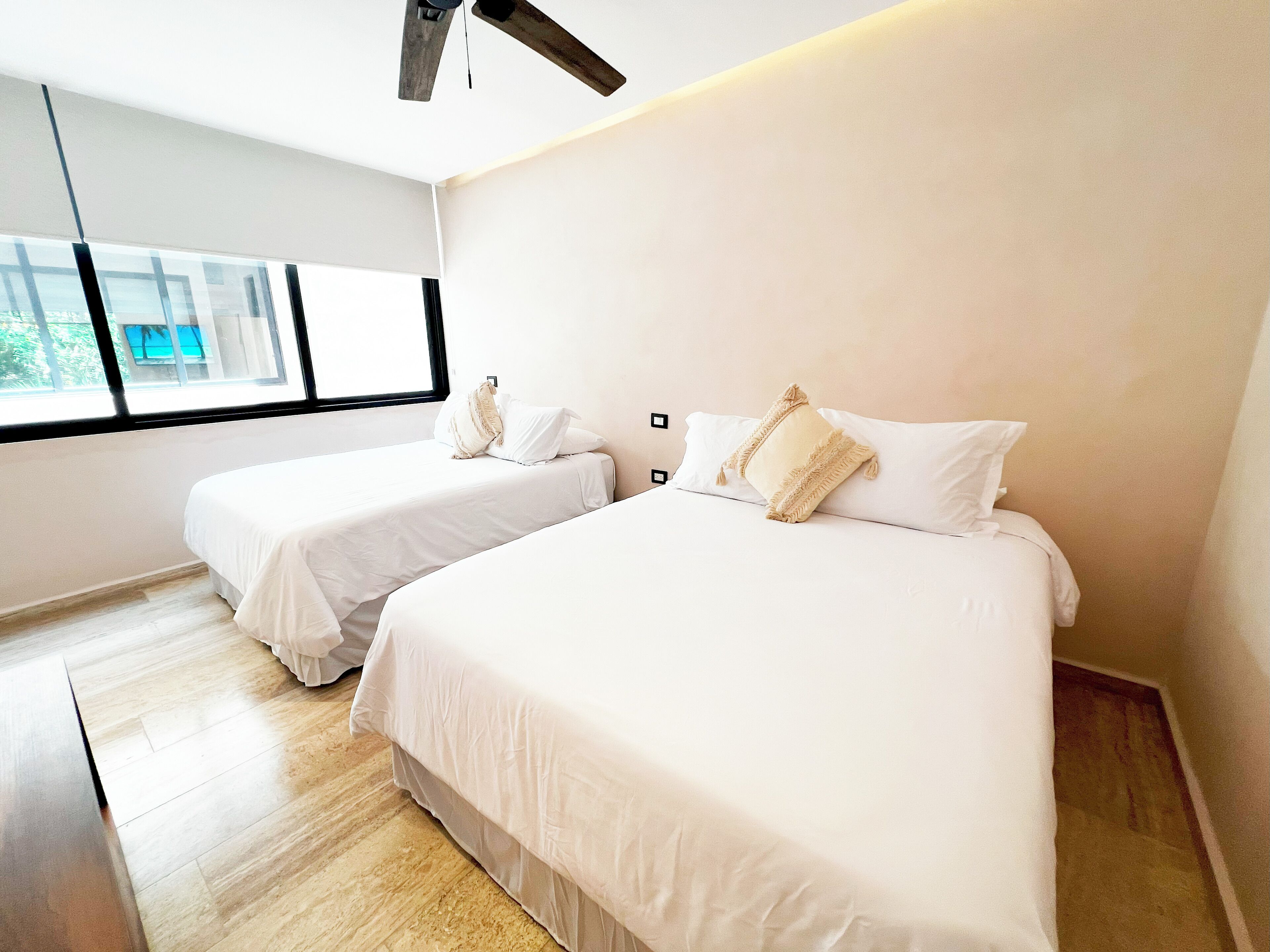 Une chambre d’hôtel moderne avec deux lits, une grande fenêtre et un ventilateur de plafond.