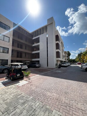 A modern building with a brick-paved courtyard, parked cars, and a golf cart. - Modern Condo Jungle Retreat (Puerto Aventuras)