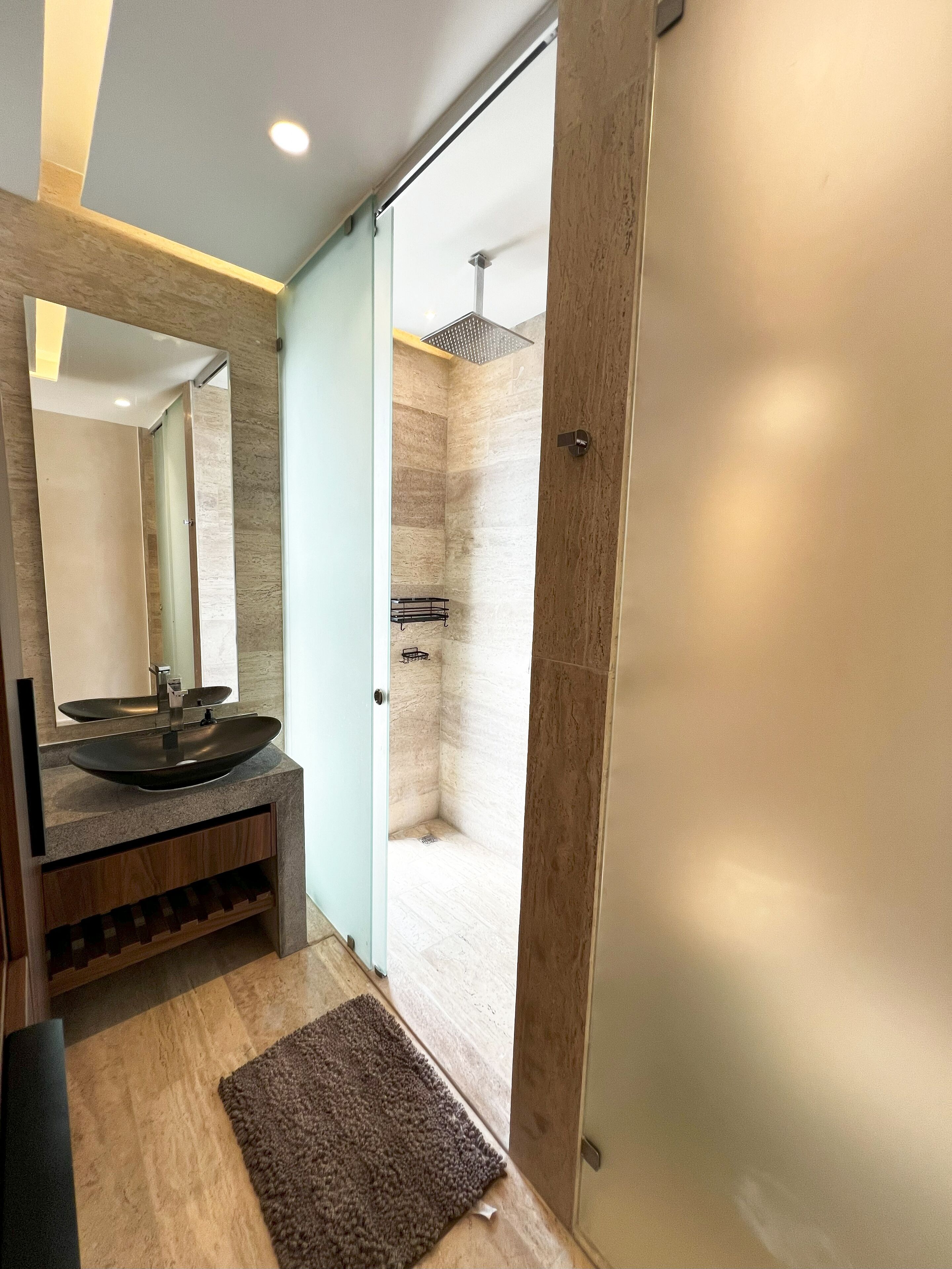 Un baño moderno con un espejo grande, un lavabo redondo, una ducha con rociador cuadrado y suelo de madera.