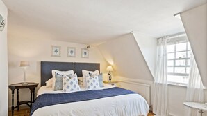 Un dormitorio con una cama grande, una mesita de noche, una lámpara, una ventana con cortinas y un radiador.