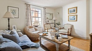 Una sala de estar acogedora con un sofá, dos sillones, una mesa de centro y una ventana con cortinas.