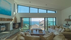 A spacious living room with a large sofa, a fireplace, and a view of the sea. - Stylish coastal retreat with panoramic views & walkable to harbour (Mevagissey)