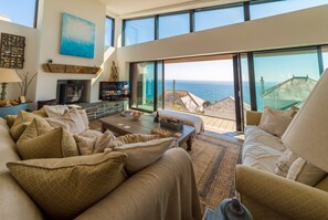 A spacious living room with a large window overlooking the sea, a fireplace, and a cozy seating area.