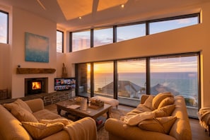 Un salón amplio con chimenea, televisor y un ventanal con vistas al mar.