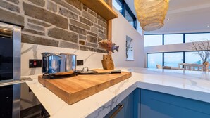 Una cocina moderna con pared de piedra, encimera de madera, una olla, un cuchillo e iluminación colgante.