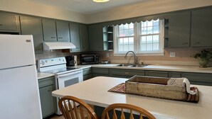A compact kitchen with a refrigerator, microwave, stove, and sink. There is a window with a view of the outside, and a small island with chairs. - Quaint Village 4 bedroom home in Friendship IN (Versailles)