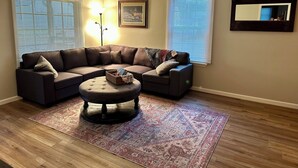A living room with a sectional sofa, a round ottoman, a patterned rug, and two floor lamps. - Quaint Village 4 bedroom home in Friendship IN (Versailles)