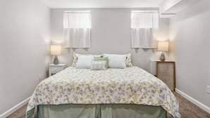 Un dormitorio con edredón estampado con motivos florales, dos lámparas de noche y una mesita de noche.