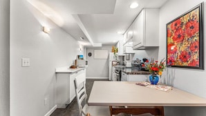 Una cocina compacta con armarios blancos, una mesa de comedor y un jarrón con flores.