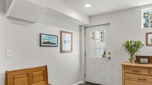 Un pasillo con un banco de madera, una puerta blanca y un aparador de madera con cajones.