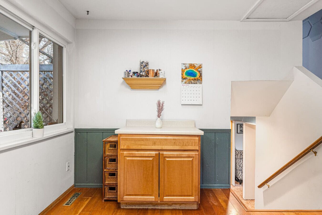 A kitchen with a wooden cabinet, a small potted plant, and a calendar on the wall.