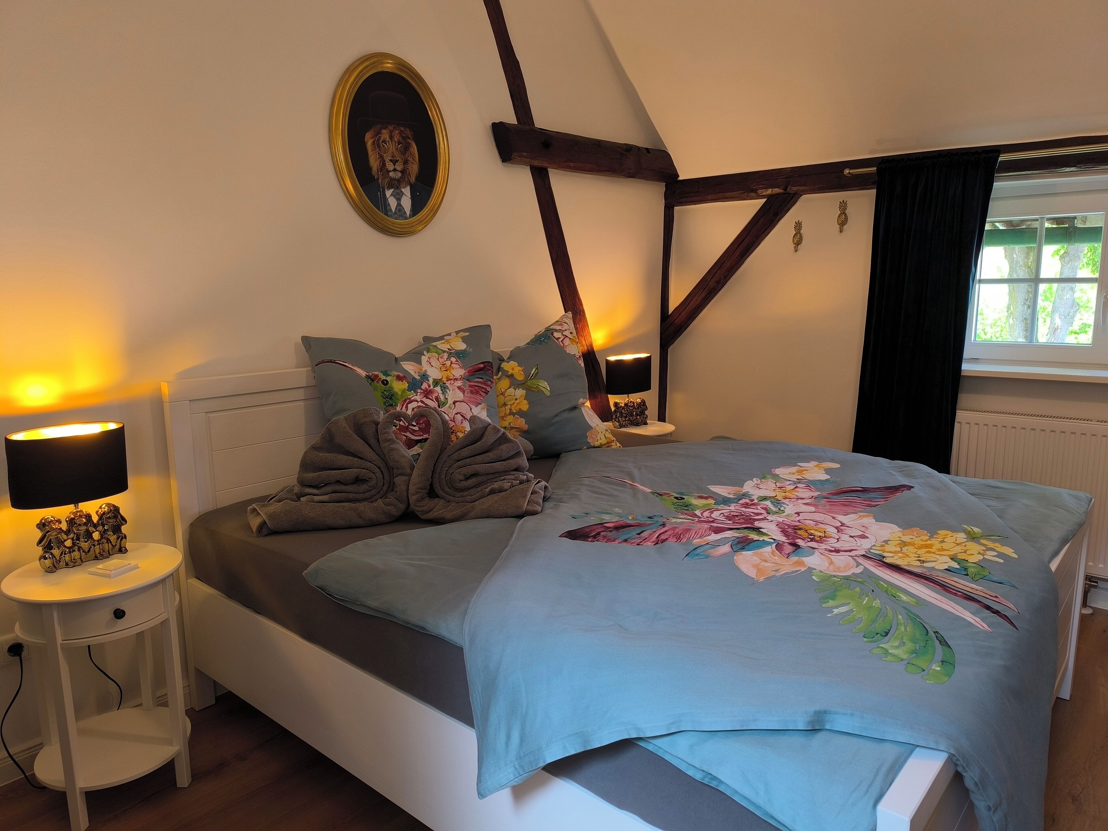 A bedroom with a bed, a nightstand, a lamp, a floral bedspread, and a framed picture on the wall.