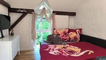 Un dormitorio con cama, mesita de noche, ventana con cortinas y estructura de vigas de madera.