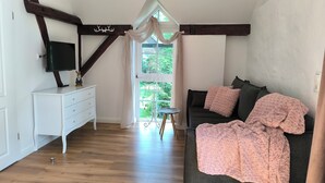 Een slaapkamer met een donkere bank, een witte dressoir, een televisie en een raam met gordijnen.
